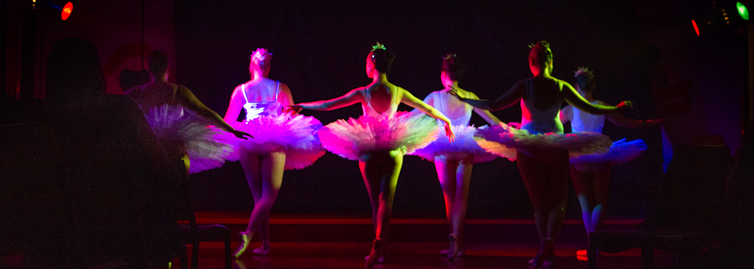 ballet dancers in a row facing the back with rainbow stage lights