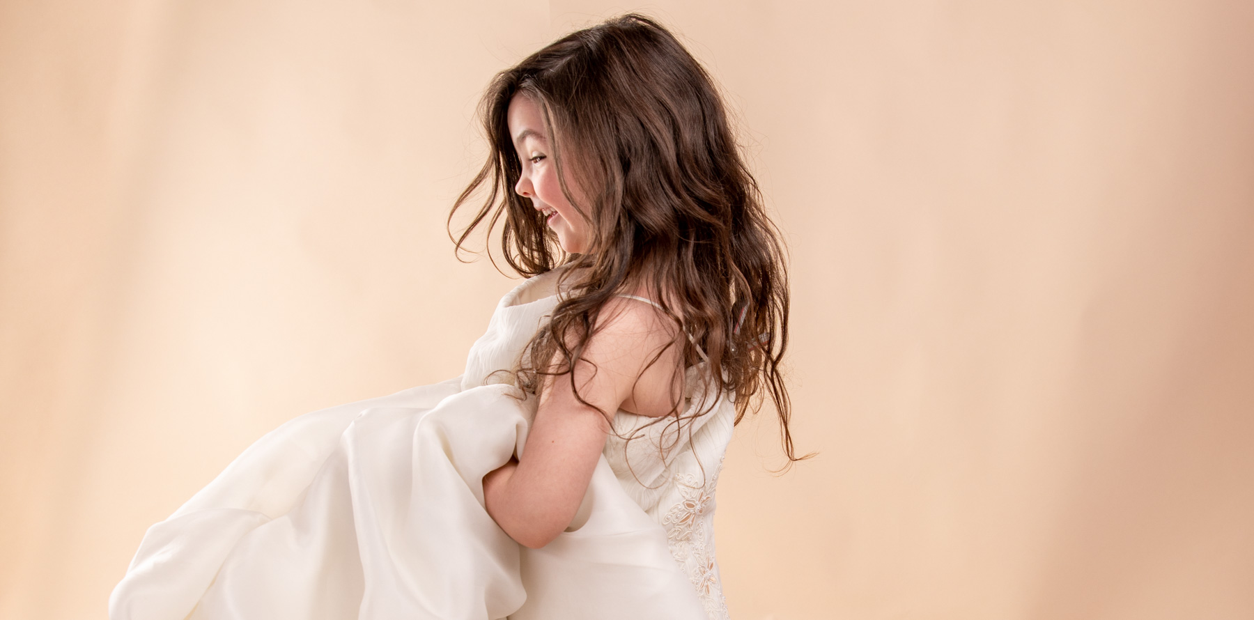 young girl in her mothers wedding dress on a cream studio background